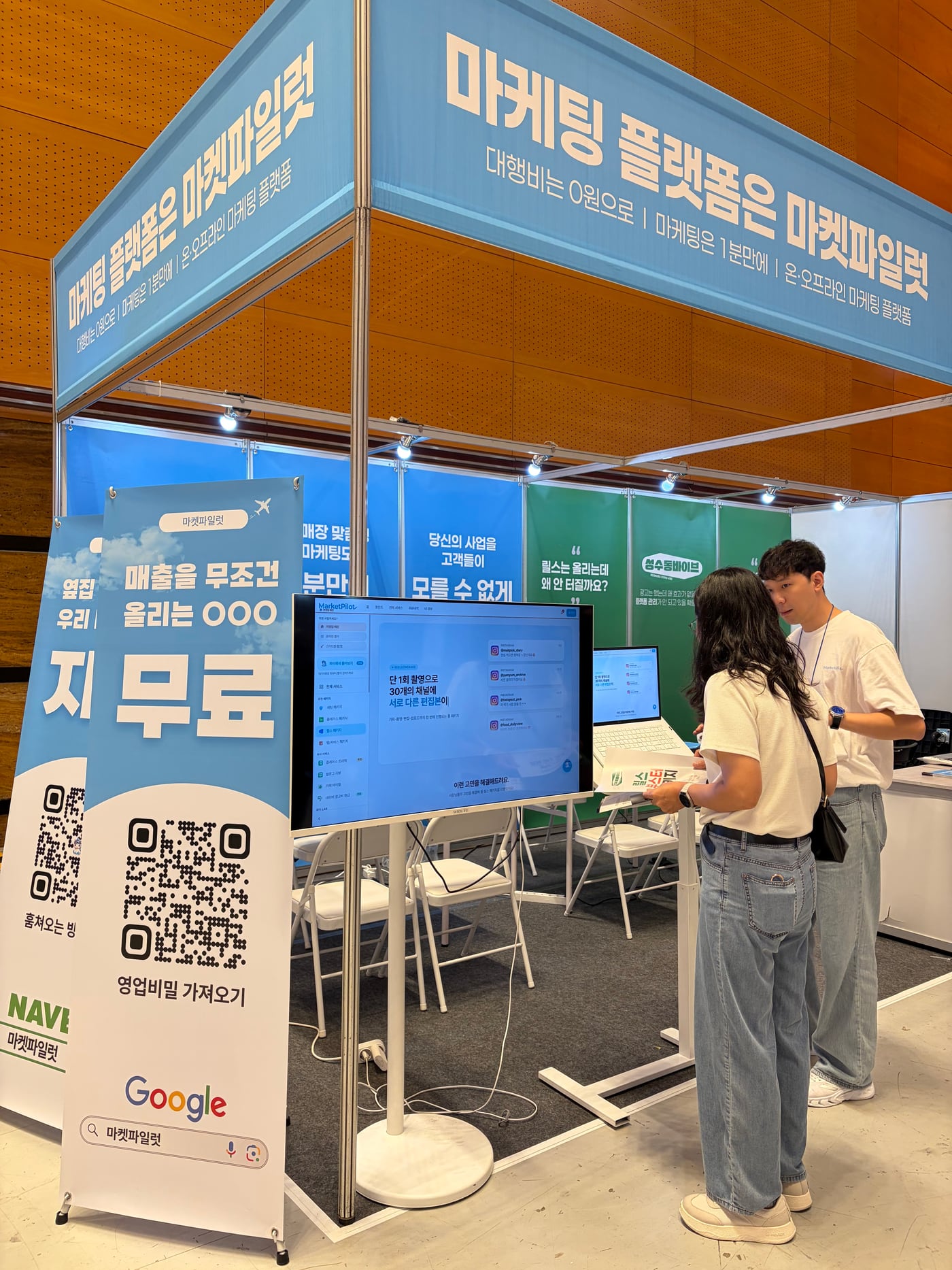무료를 크게 쓴 QR 입간판과 통로 쪽 시연 모니터, 뒤쪽 거치대 위 노트북